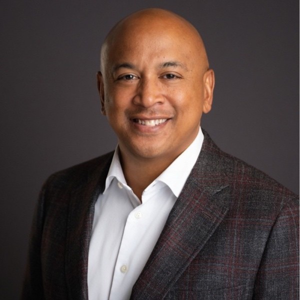 Speaker at a business conference, wearing a suit and smiling.