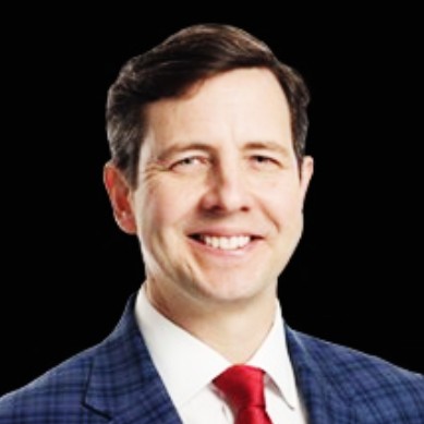 Speaker at a conference, wearing a suit and tie.