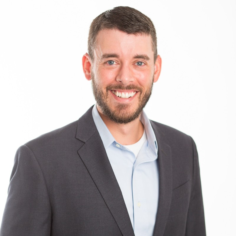 Speaker at a business conference, smiling in a suit.