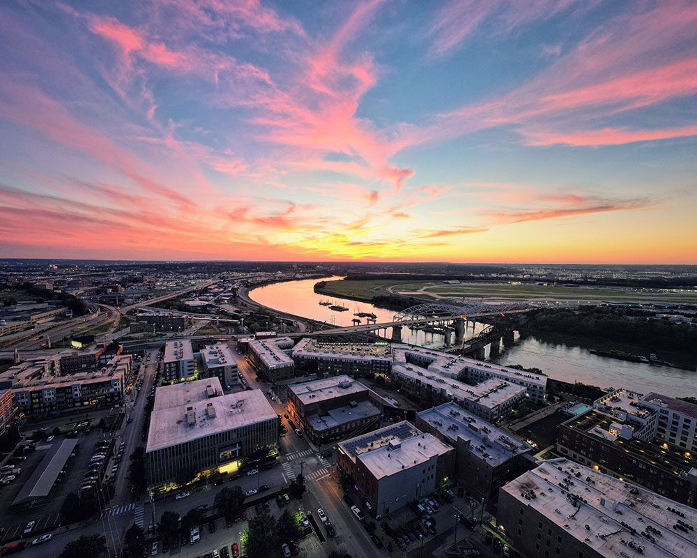 Aerial view of a city venue at sunset with a river and colorful sky.